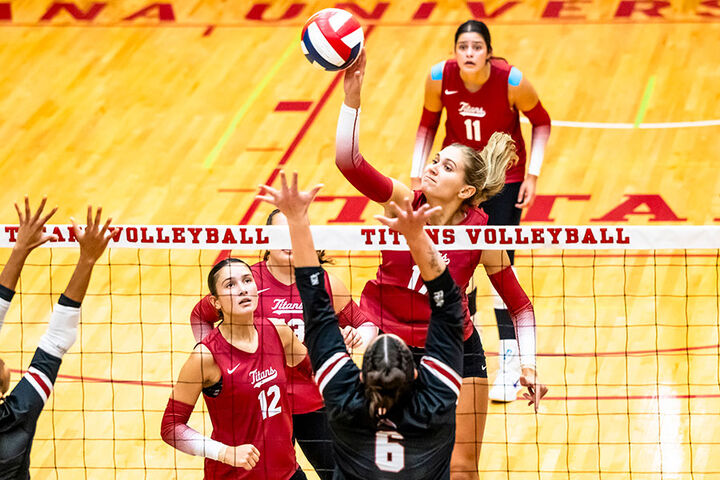 Female volleyball player is at the net spiking the ball.